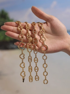 Gros plan de bracelets dorés avec zircons 5A et breloques en cœur sur la plage ensoleillée