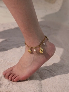 Dettaglio di ciondoli a conchiglia dorata e perle su una cavigliera su sfondo di spiaggia