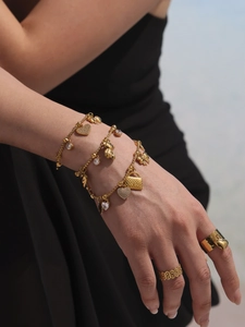 Details eines goldfarbenen Herz-Armbands mit Zirkonia-Anhängern und Ringen am Model