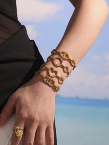 Détail de bracelets multicouches dorés sertis de zircons dans un décor de plage