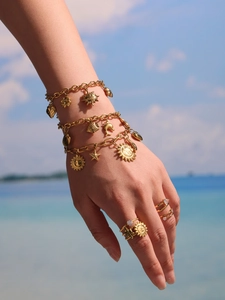 Bracelet doré aux breloques marines avec soleil et dauphin porté à la plage
