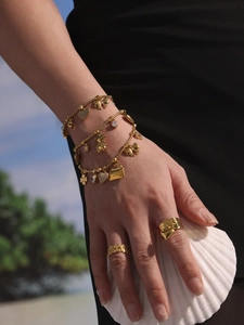 Detail von vergoldetem Edelstahl-Armband mit Anhängern und Ringen am Strand