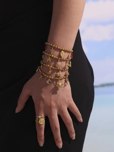 Detail of gold beaded bracelets and sun charm ring set against beach background