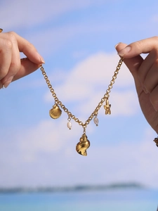 Bracciale oceanico dorato con perle d'acqua dolce e ciondoli conchiglia su sfondo spiaggia