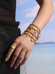 Detail of gold charms with sea turtle, bee, and butterfly on a multi-layer beaded bracelet
