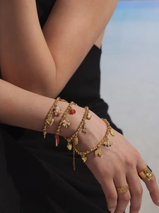 Detail of stacked gold charm bracelets with heart, bear and clover charms on a model