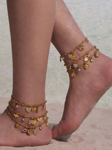 Detaillierte Ansicht goldener Fußkettchen mit Herz- und Bogendesign am Sandstrand