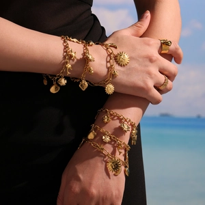 Bracelet doré multi-breloques avec pendentifs soleil et coquillages sur la plage