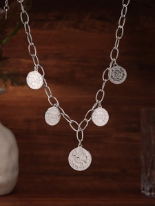 Dettaglio della collana a catena d'argento con cinque ciondoli a moneta su legno scuro