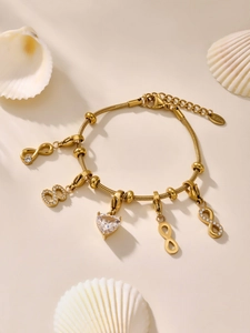 Dettaglio del bracciale dorato in acciaio inox con zircone a cuore e ciondoli infinity