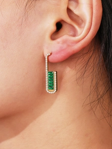 Detail of luxury geometric gold drop earrings with emerald-cut green stones and pavé zircons