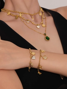 Detail van gelaagde gouden ketting en armband set met vlinder- en vogelhangers