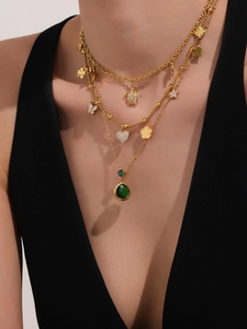 Detailweergave van gelaagde gouden ketting met vlinder, ster en smaragdgroene hanger