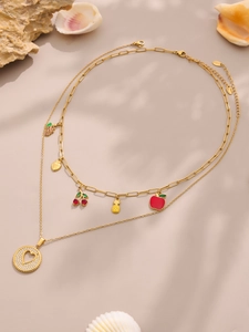 Detalle de collares dorados en capas con dijes de frutas de esmalte sobre un fondo de arena