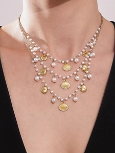 Detailed view of layered necklace with gold shell pendant and elegant white pearls