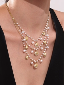 Detail view of multi-layered gold necklace with shell charms and pearl tassels on a model
