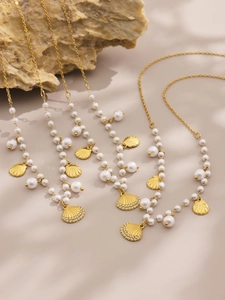 Macro detail of gold necklaces featuring white pearls and shell pendants on a textured stone