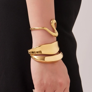 Conjunto de brazaletes dorados minimalistas ondulados y anchos en la muñeca de una modelo