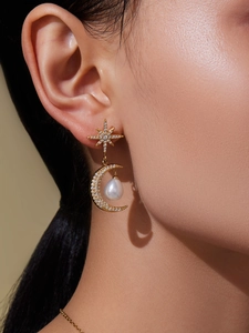 Détail de boucles d'oreilles dorées avec étoiles, lunes, zircons et perles pendantes