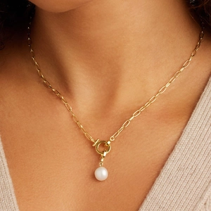 Detail van gouden paperclip ketting met een ronde sluiting en witte parelhanger