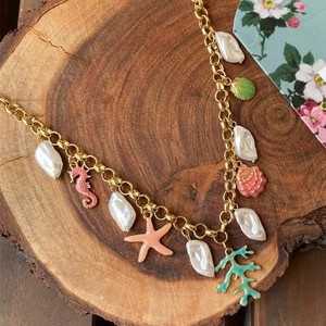 Gold chain necklace with baroque pearls and colorful enamel ocean charms on wood