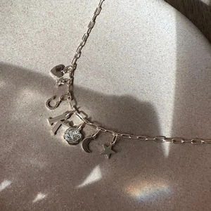Silver steel paperclip necklace with heart, rose, and moon charms on beige base