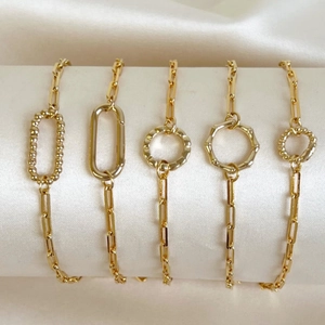 Détail de cinq bracelets chaîne trombone dorés avec divers designs de maillons géométriques