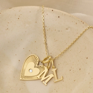 Detailopname van gouden ketting met hart- en letterhangers M en L op een keramische schaal