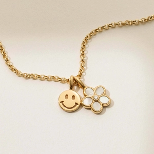 Detail of gold necklace featuring a classic smiley face and white shell flower pendant