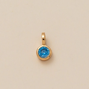 Detailed close-up of a gold pendant featuring a round blue zircon gemstone setting