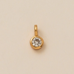 Close-up of a circular gold bezel-set pendant featuring a clear brilliant-cut zircon gem