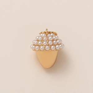 Macro shot of 18K gold acorn pendant with white imitation pearls on beige background