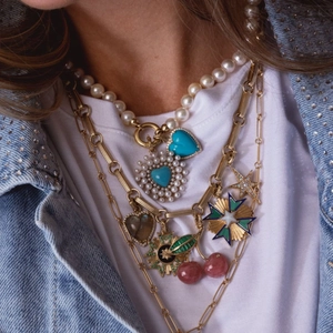 Layered gold chain necklace featuring pearls and cherry pendants on a denim jacket model