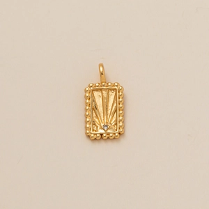 Détail macro d'un pendentif rectangulaire doré avec rayons de soleil et petit zircon