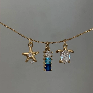 Detail of gold necklace with sea star, zircon column, and sea turtle charms