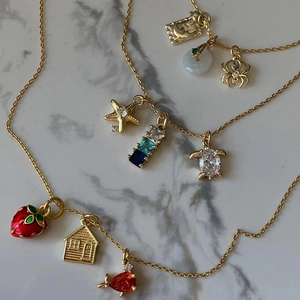 Detailed view of gold layered necklaces featuring strawberry and spider charms on marble