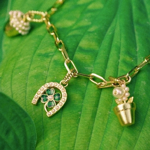 Macro shot of horseshoe and plant charms on a golden link chain bracelet over green leaves