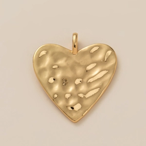Gros plan d'un pendentif coeur doré avec une texture martelée unique et un anneau poli