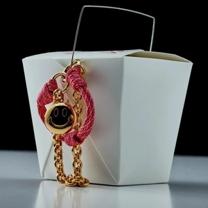 Detail view of pink braided cord and gold chain with a smiley face metal charm