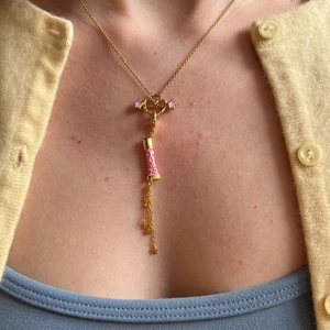 Detailansicht der 18K vergoldeten Halskette mit rosa Emaille-Rohr und Stern-Quasten am Modell