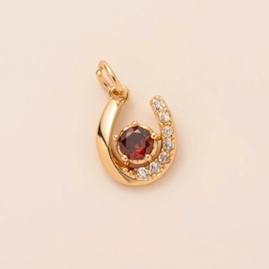 Macro shot of gold-plated horseshoe pendant with red gemstone and cubic zirconia