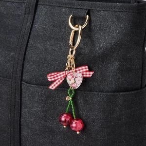 Handmade cherry keychain with red spheres and a red checkered bow on a black canvas bag