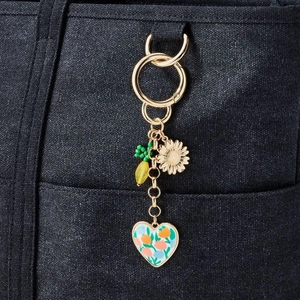 Detail of 18K gold plated keychain with sunflower and floral heart charm on navy bag