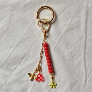 Detail showing 18K gold-plated keychain with red beads, bee charm, and heart pendant