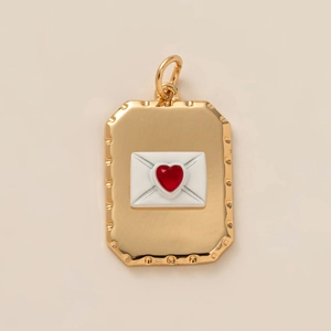 Close-up of gold envelope pendant featuring white enamel and a red heart gemstone