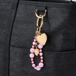 Detail of 18K gold heart pendant with pink beaded chain on a black canvas bag