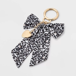 Detail of leopard print fabric bow keychain with golden spring clasp and heart charm