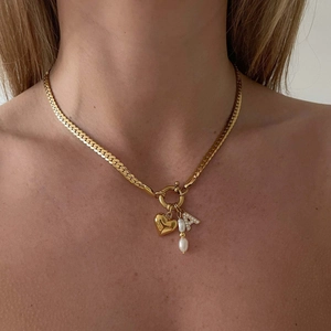 Detailopname van gouden Cubaanse schakelketting met hart-, parel- en letter A-hangers