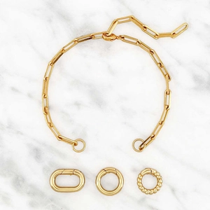 Gold plated paperclip link chain necklace with three interchangeable charms on marble background