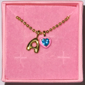 Dettaglio di una collana a sfere dorate con ciondolo lettera A e cuore in zircone blu